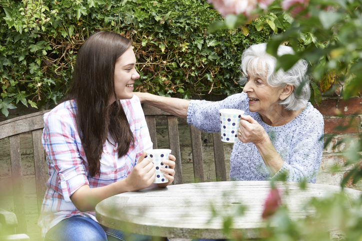 Teenage Granddaughter Relaxing With Grandmother In Garden
